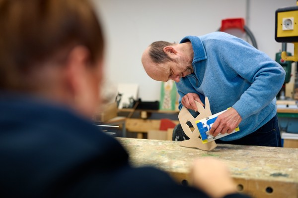 Ein Mann feilt an einem Holzstück.