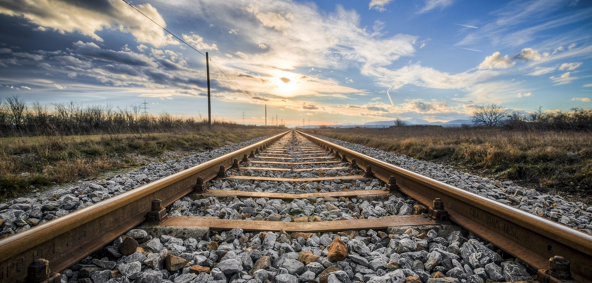 Eine Nahaufnahme zeigt ein Bahngleis vor einem wolkenverhangenen Himmel in den fernen Horizont verschwinden