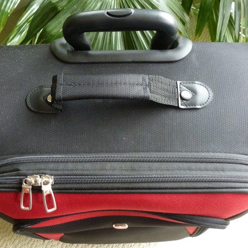 Ein grauer Koffer mit Tragegriff und rotem Reißverschluss.