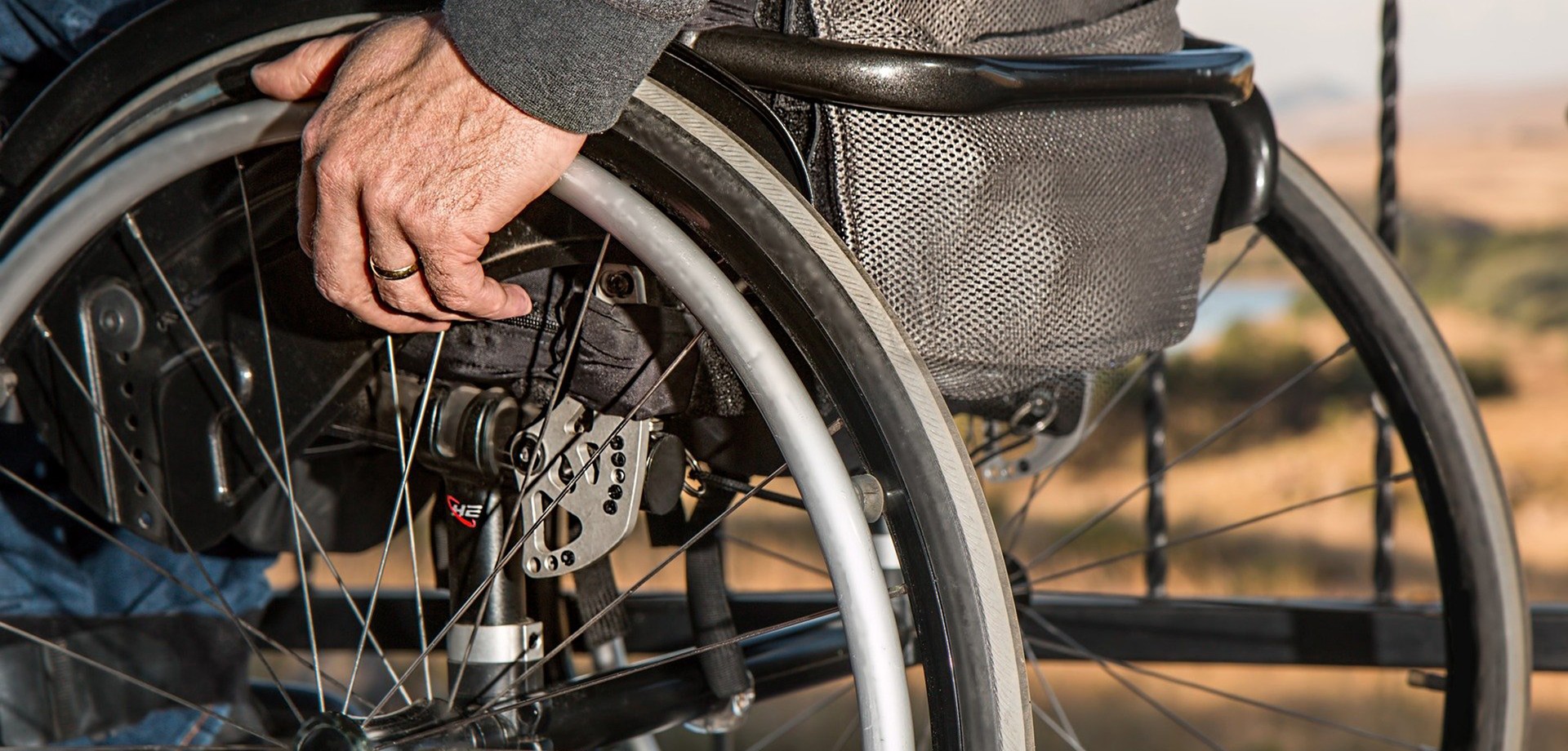 Ein Mensch sitzt in einem Rollstuhl und fasst mit der linken Hand ein Rad an