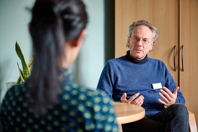 Ein Mann im blauen Pullover spricht mit einer Frau mit dunklem Pferdeschwanz.