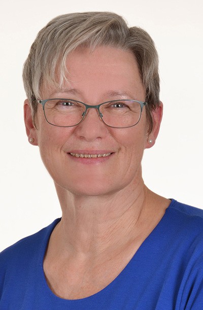 Eine lächelnde Frau mittleren Alters mit kurzen grauen Haaren und einer Brille