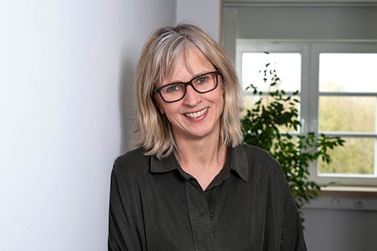 Eine Frau mit schulterlangen blonden Haaren und einer dunklen Brille lächelt. Foto: Henrike Hochschulz