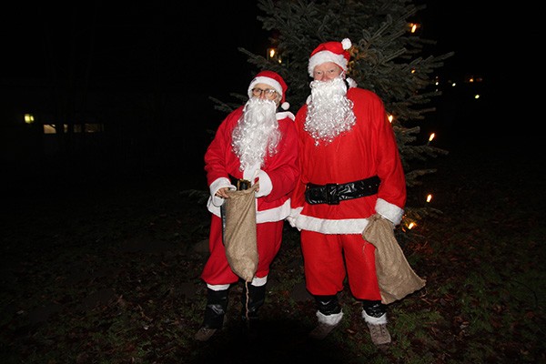 Eine Frau und ein Mann in Nikolauskostümen stehen vor einem beleuchteten Weihnachtsbaum