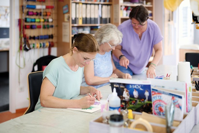 drei Personen sitzen am Tisch und machen etwas Kreatives