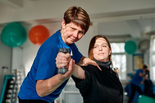 Eine Frau hilft einer anderen Frau, den Arm mit einer Hantel auszustrecken