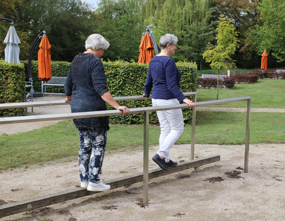 Zwei Frauen balancieren auf einer Stange und halten  sich an einem Geländer fest.