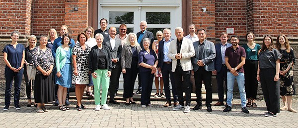 Eine Gruppe von etwa 25 Menschen steht vor einem roten Backstengebäude mit einer weißen Tür
