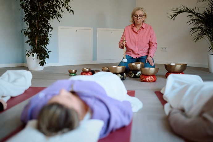 Frauen liegen auf dem Rücken, eine Frau spielt auf Klangschalen