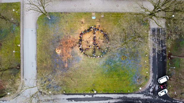 Eine Menschengruppe stellt auf einer Rasenfläche das Friedenszeichen