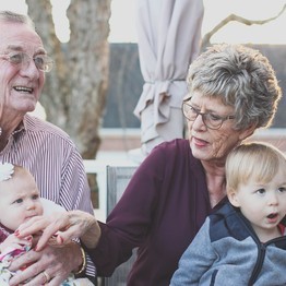 Zwei kleine Kinder sitzen jeweils auf dem Schoß eines älteren Mannes und einer älteren Frau, die lächeln