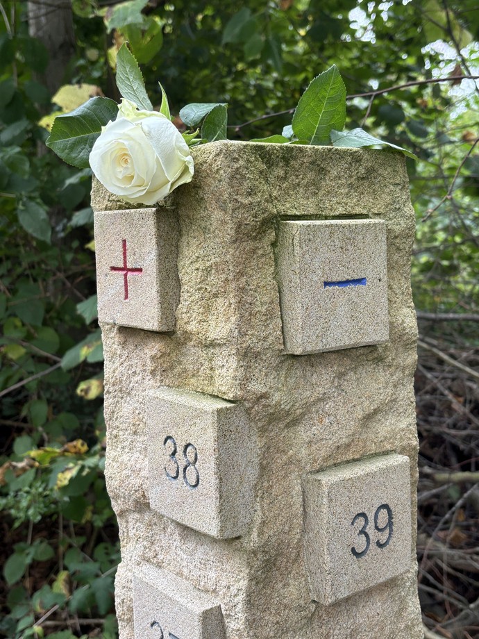 ein Gedenkstein mit Quadraten, von denen eins ein rotes Pluszeichen, eins ein blaues Minuszeichen, eins die Zahl 38 und eins die Zahl 39 zeigt