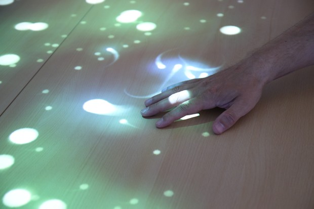 Eine Hand wischt über helle, bunte Lichtreflexe auf einem Tisch