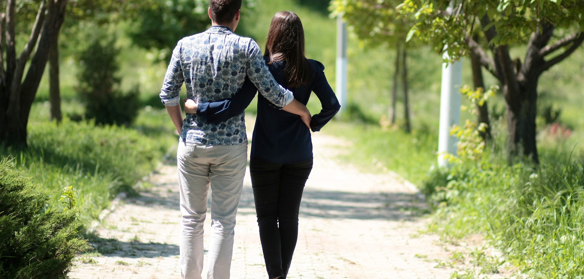 Eine Frau und ein Mann gehen durch einen Park. Sie haben jeweils einen Arm um den anderen gelegt