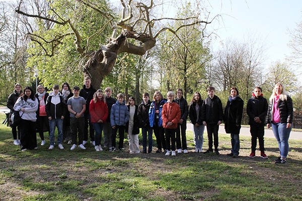 16 junge Menschen und vier erwachsene Frauen stehen vor einem knorrigen Baum