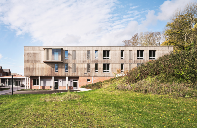 Flacher Holzbau zwischen grünem Rasen und blauem Himmel
