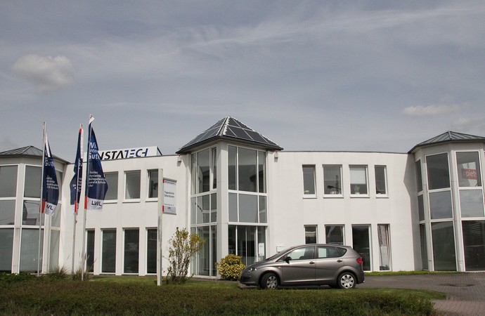 Weißes, flaches Gebäude mit Glasturm, davor ein silbernes Auto