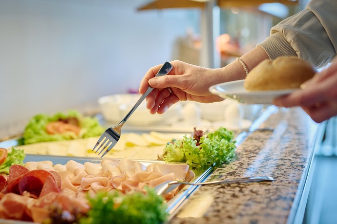 Jemand nimmt mit einer Gabel etwas vom Buffet