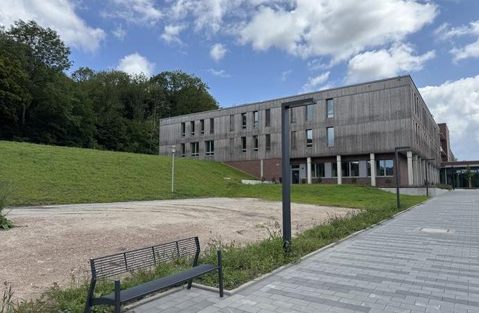 flaches Gebäude mit Holzfassade und Säulen steht auf grünem Rasen bei blauem Himmel