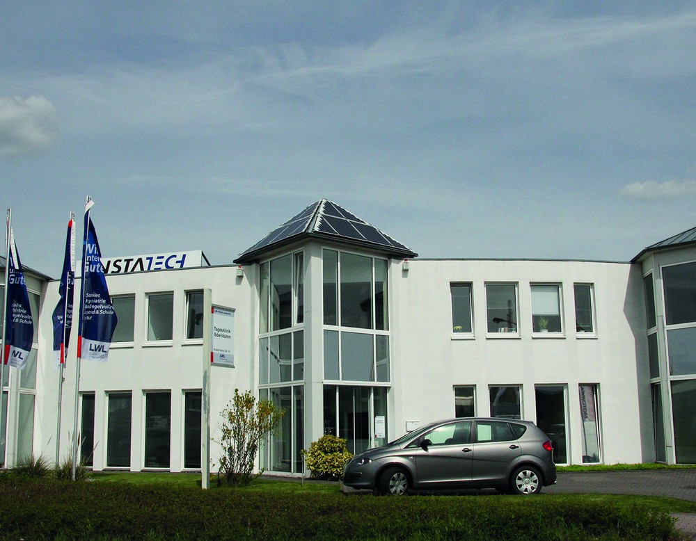 Blick auf ein weißes, zweistöckiges Haus mit großen Fenstern. Davor steht ein graues Auto, links wehen drei blaue LWL-Flaggen