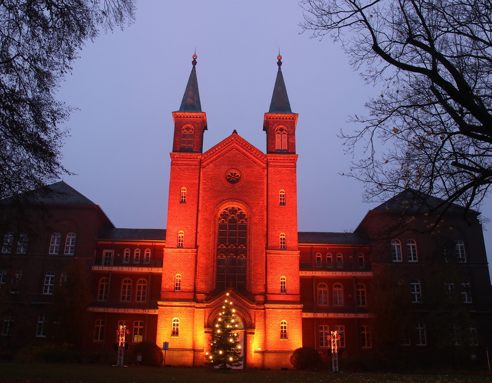 Das orange beleuchtete Klinikportal mit zwei hohen Türmen