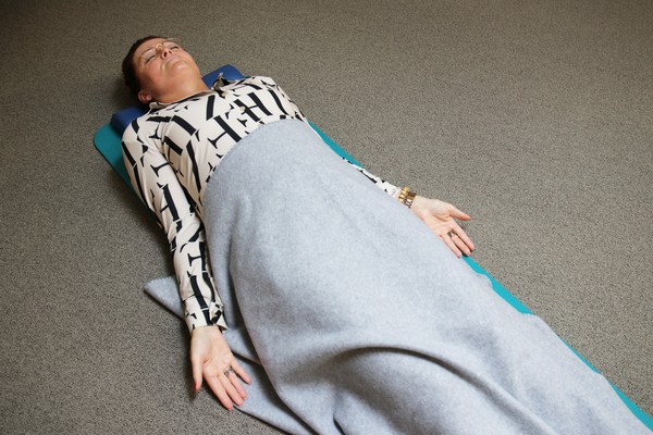 Mensch liegt auf einer Gymnastikmatte unter einer Decke