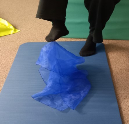 Jemand versucht mit einem Fuß ein blaues Tuch hochzuheben.